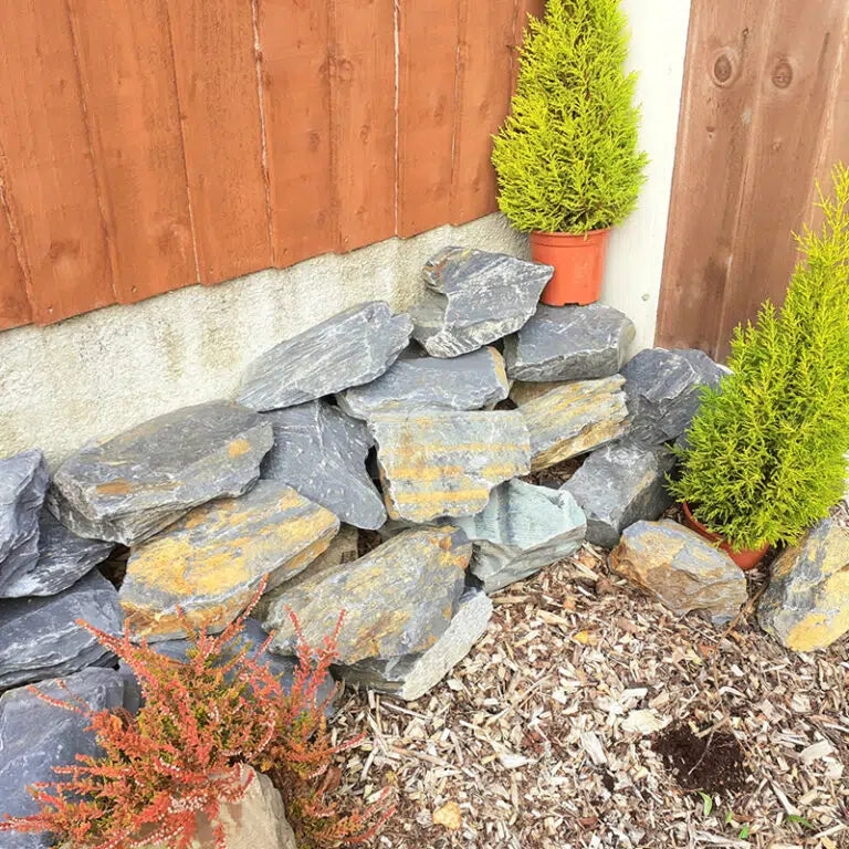 Slate rockery stones stacked beside a fence with small conifers and heathers