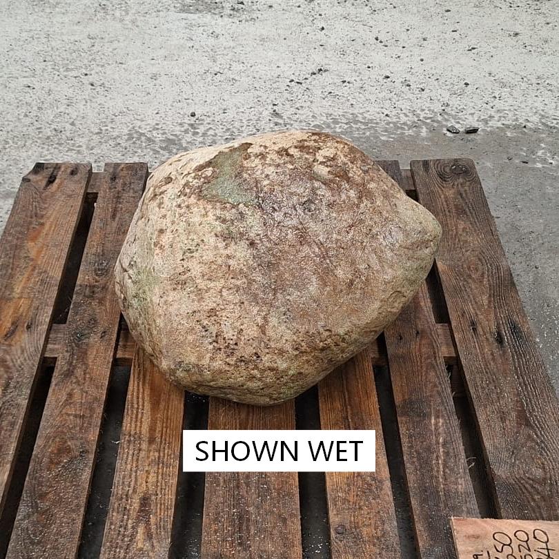 A wet glacial boulder resting on a pallet outdoor.