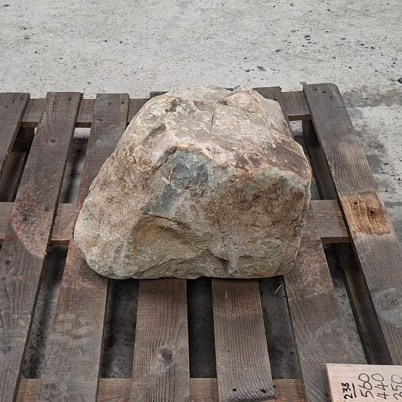 A glacial boulder with a tan, grey, and brown textured surface, resting on a weathered wooden pallet.
