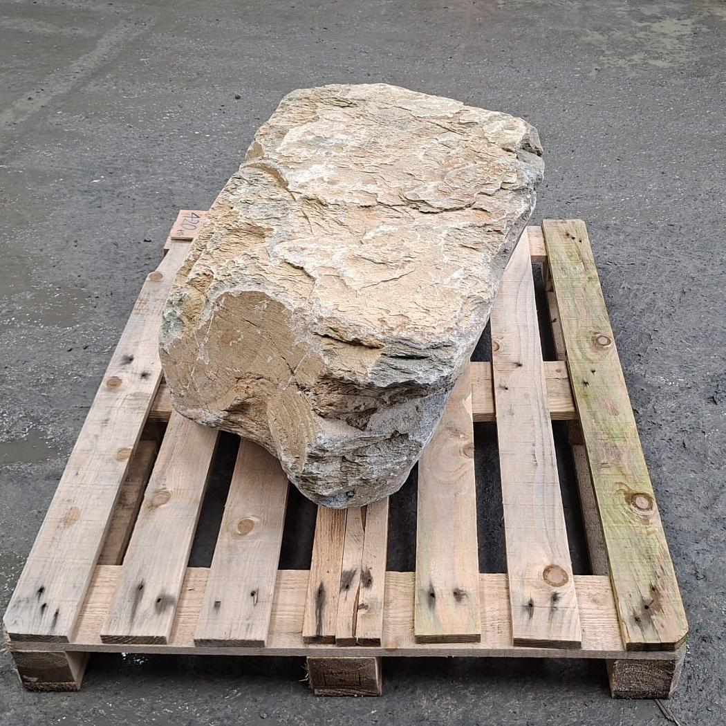 Unique stone boulder with natural colour tones on a wooden pallet, showing the rough texture and flat top surface.