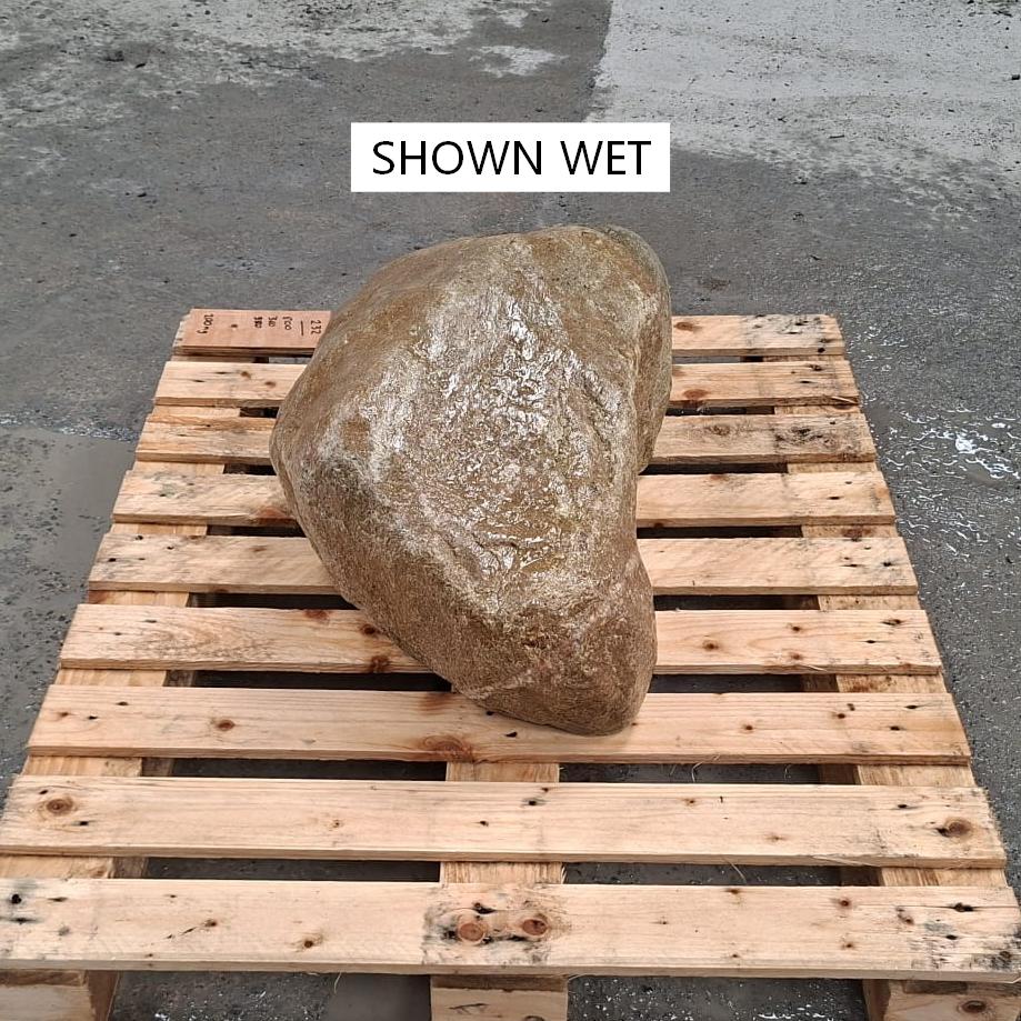 A large wet stone boulder placed on a wooden pallet outdoors.