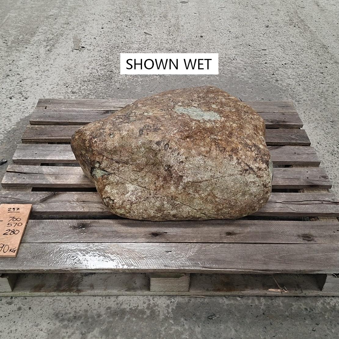 A wet glacial stone placed on a wooden pallet on a concrete floor.