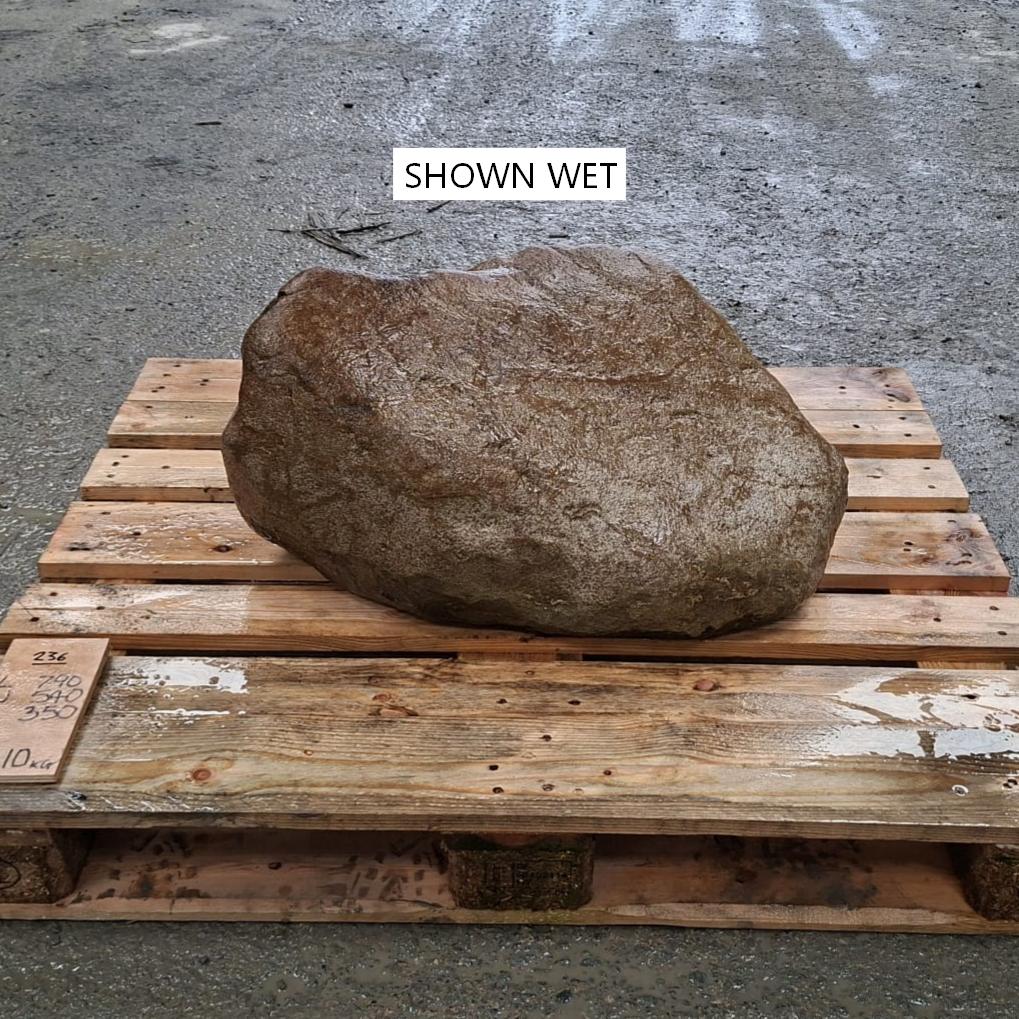 A large wet boulder or landscaping stone resting on a wooden pallet outdoors.
