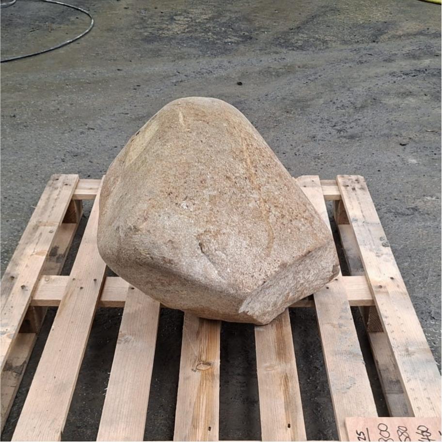 A large natural tan stone or boulder placed on a wooden pallet outdoors.