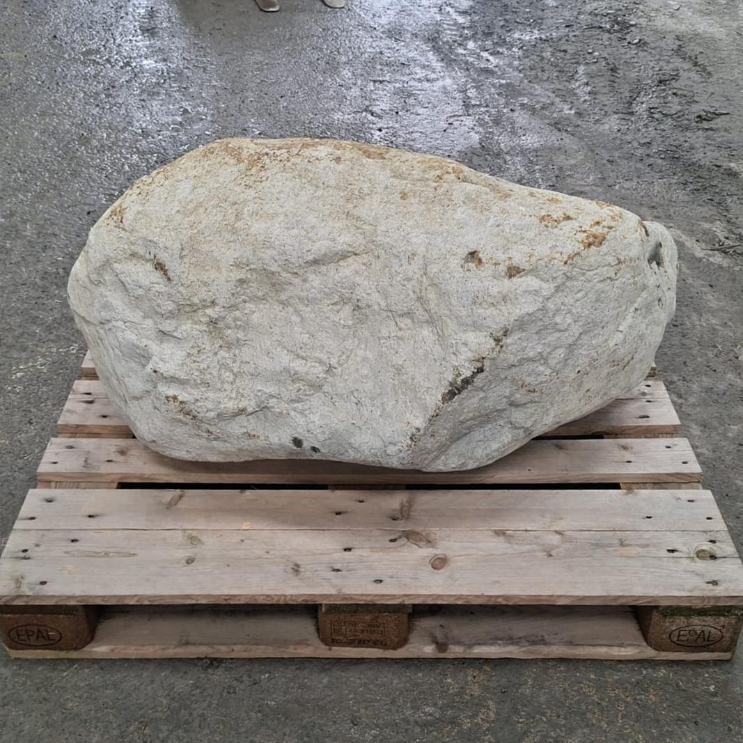 A large irregular natural stone or boulder with a rough off-white to light beige surface sits on a wooden pallet.