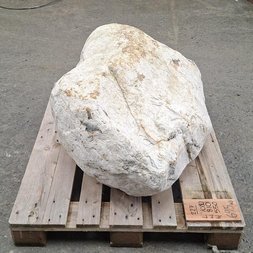 A large irregular white stone or boulder placed on a wooden pallet outdoors.