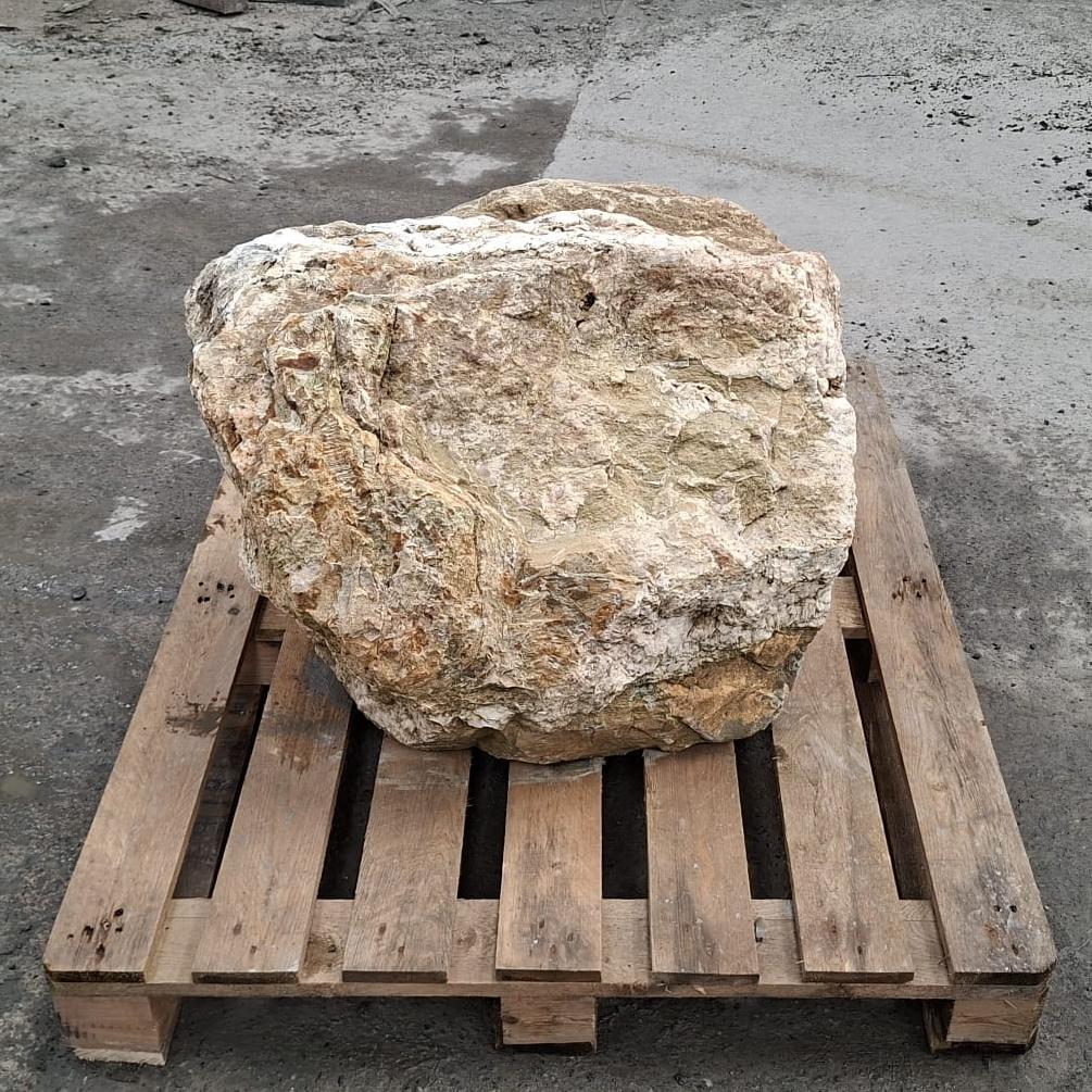 A large natural stone or boulder with rough, textured surfaces in beige, cream, and light brown tones, displayed on a wooden pallet.