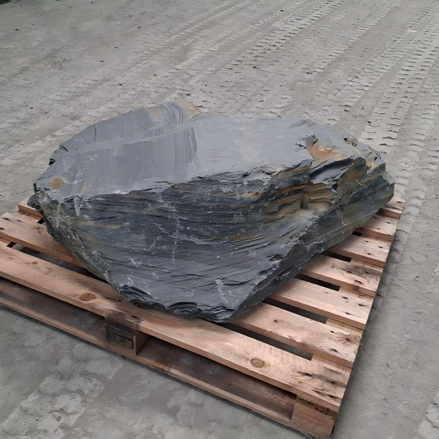 Welsh slate boulder showing a broad flat face above curved layered edges