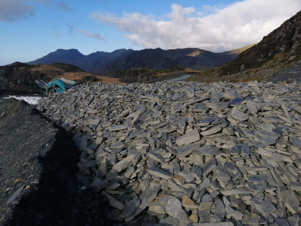 Raw Welsh slate piled at Llechwedd Quarry, Blaenau Ffestiniog, with Snowdonia mountains behind