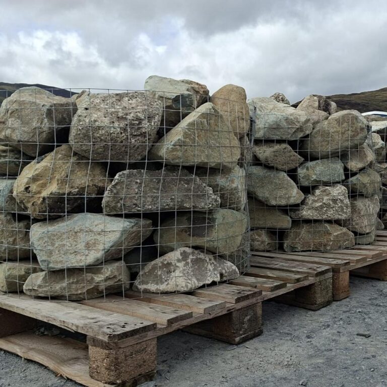 Wire cages of mixed glacial rockery stones on pallets beneath a cloudy sky