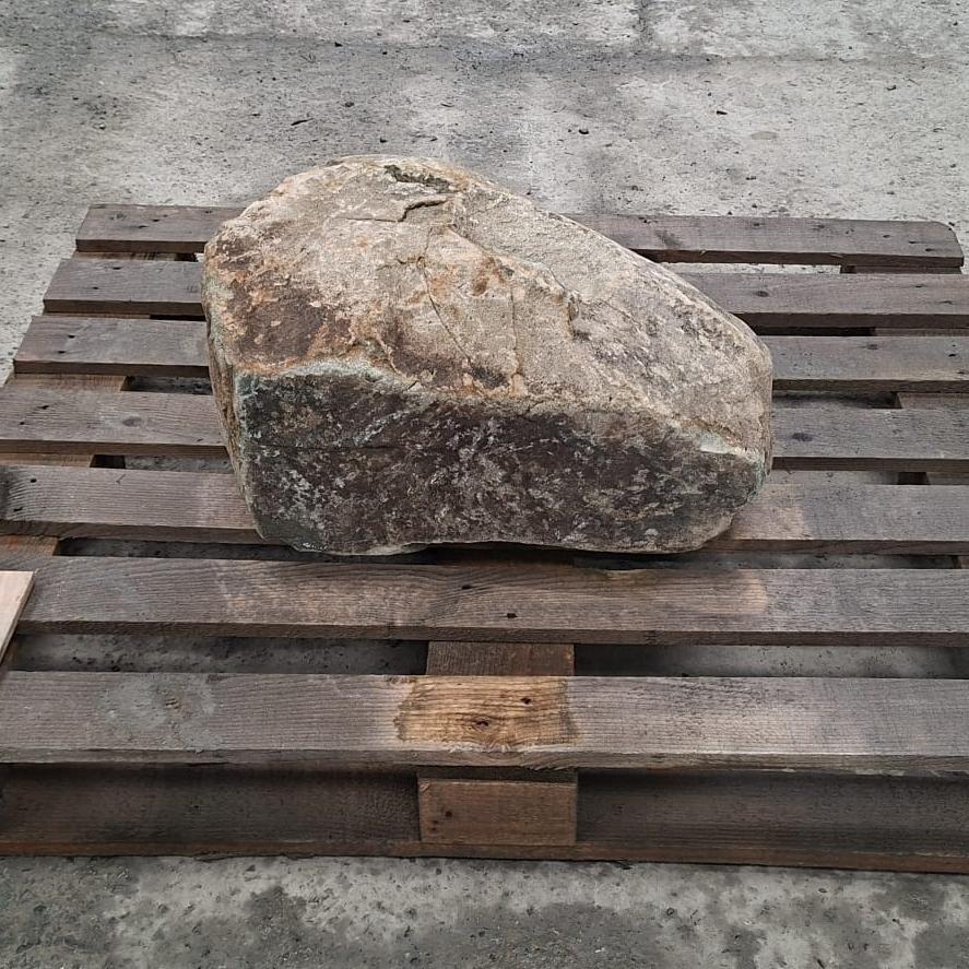 A glacial boulder with unique straight edge and rough texture, displayed on a wooden pallet.