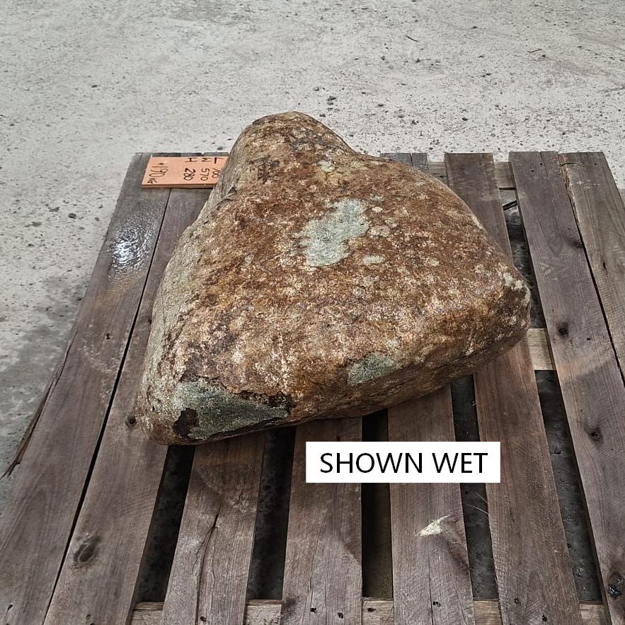 A wet glacial stone placed on a wooden pallet, with a natural unique shape and darkened earthy colours.