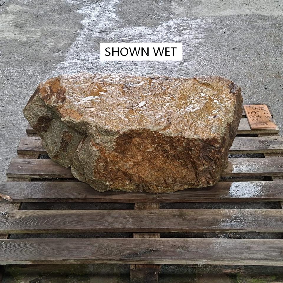 A wet stone boulder with a flat top, shown wet and with natural and varying colour tones.