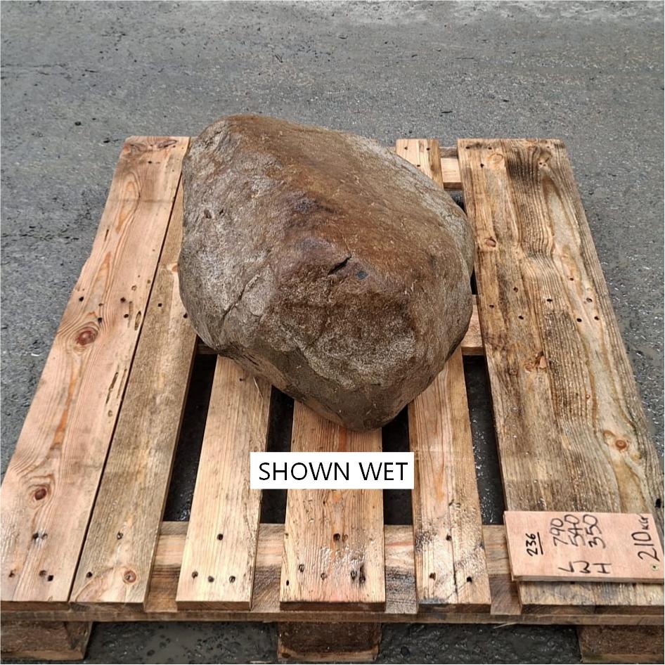 A large wet boulder placed on a wooden pallet outdoors.