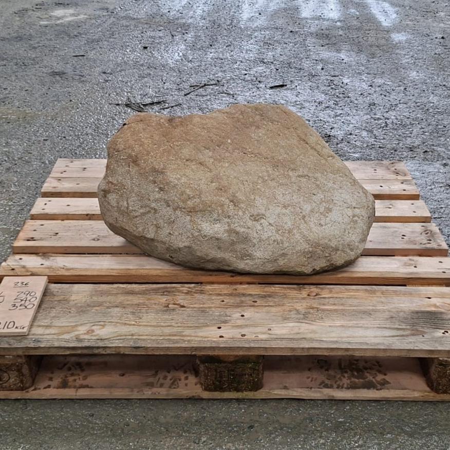 A large natural tan stone or boulder displayed on a wooden pallet outdoors.