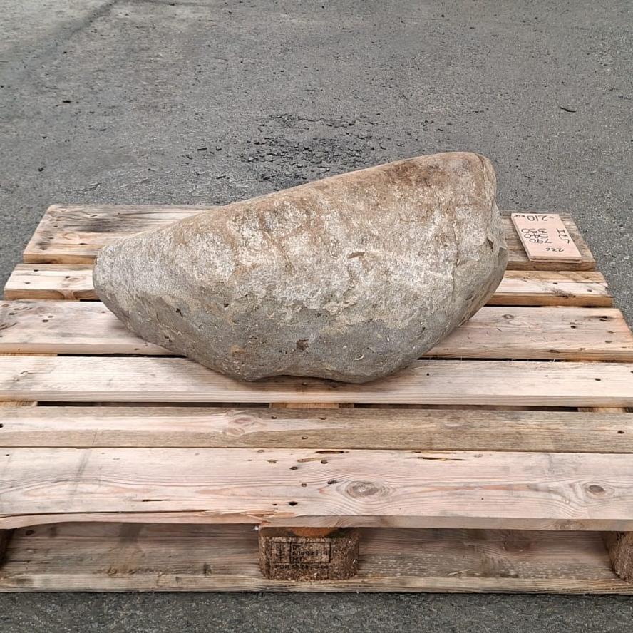 A large natural stone with a textured surface sits on a wooden pallet outdoors.