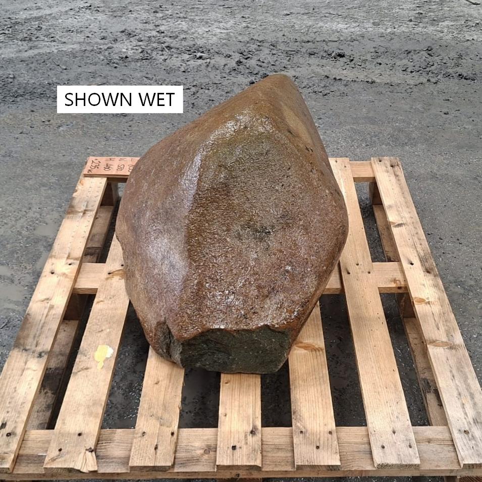 Glacial stone boulder with irregular shape, sitting on a wooden pallet. Boulder is wet, showing the darkened colouring.