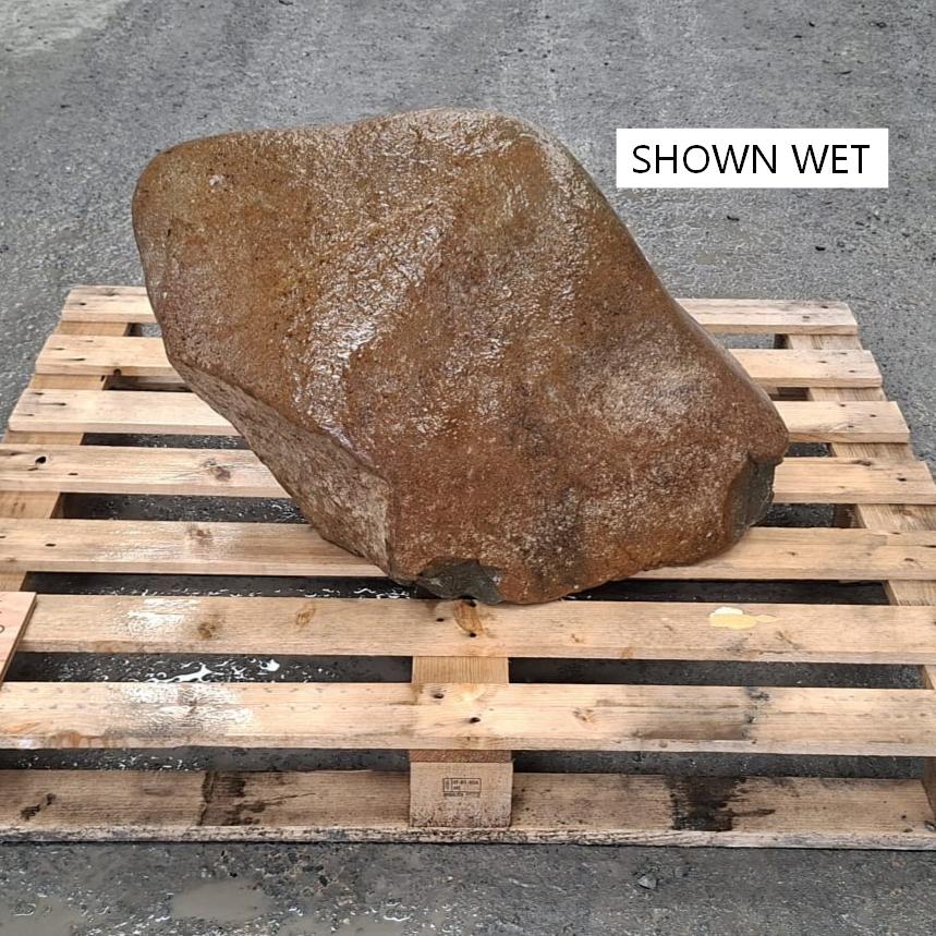 A wet glacial stone boulder with irregular shape, sitting on a wooden pallet.