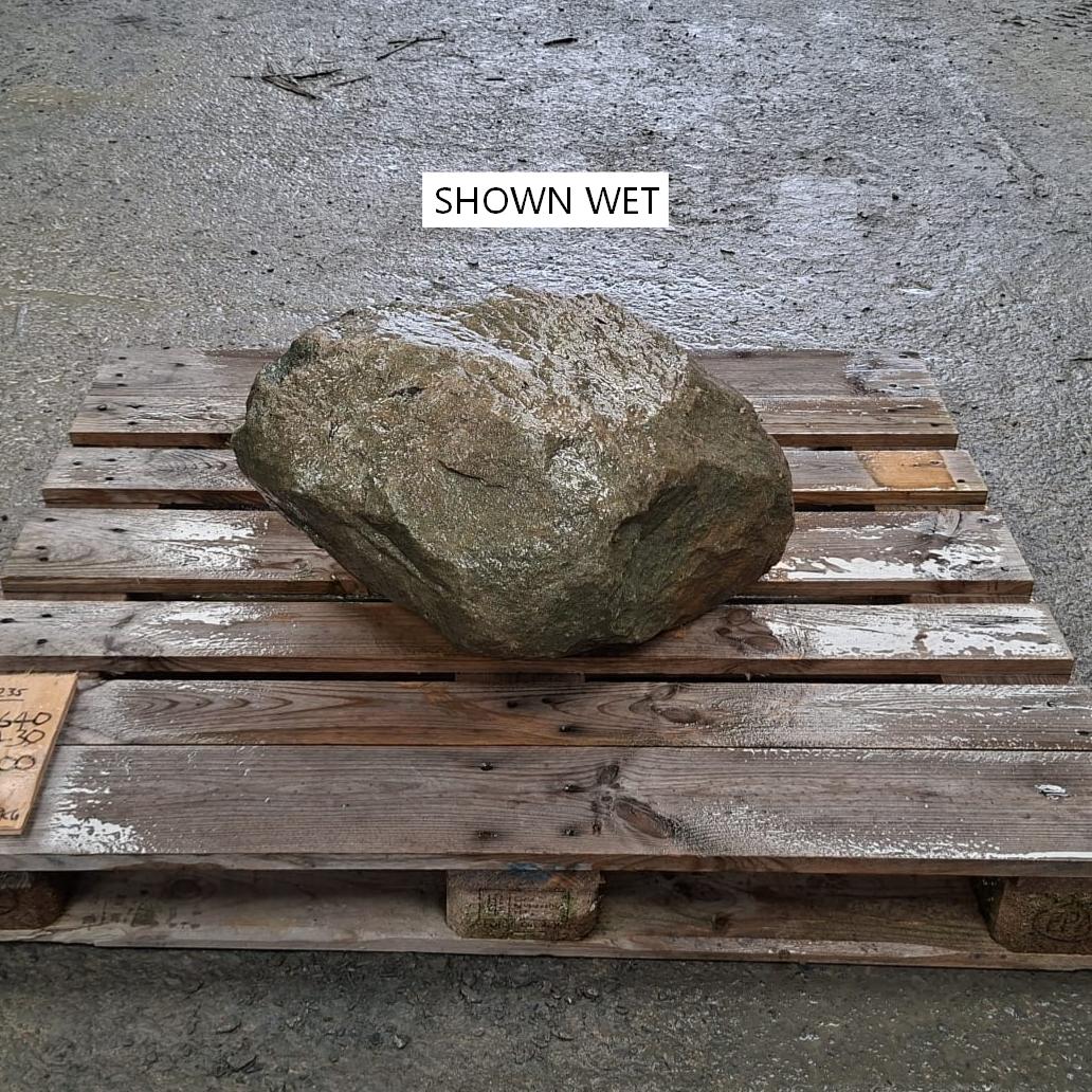 A wet boulder placed on a wooden pallet over a concrete surface.