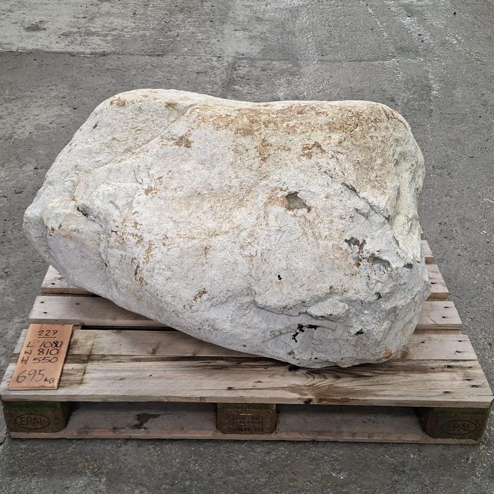 A large irregular white stone or boulder with natural beige and brown weathering, displayed on a wooden pallet over.