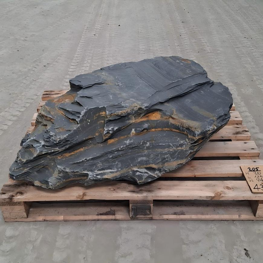 Welsh slate boulder showing sweeping dark layers separated by rusty bands
