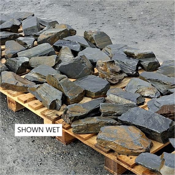 Wet Welsh slate pieces spread across pallets, showing angular shapes
