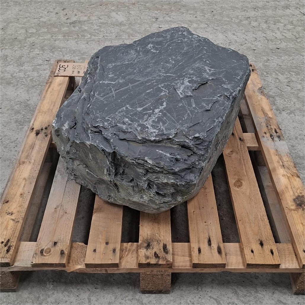 A large rough dark gray stone or boulder with natural striated texture, displayed on a wooden pallet.