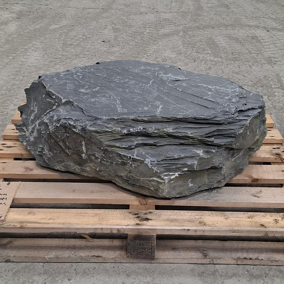 A large irregular dark grey stone boulder with visible layered texture, resting on a wooden pallet.